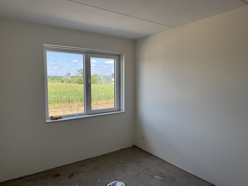 Kale slaapkamer in een nieuw huis aan de dorpsrand, met uitzicht op een maisveld